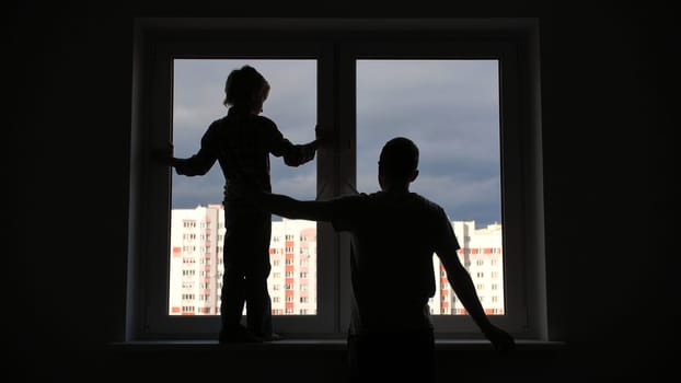 Silhouette of a father with his son against the background of a window to the apartment