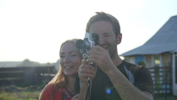 A young guy next to his girlfriend is filming a video on a retro video camera from the 60s