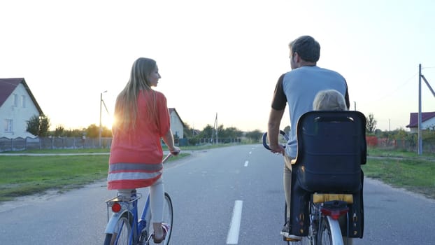 Young couple on a bike with their little daughter at sunset