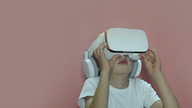 A little boy is watching a video in virtual glasses on a pink background