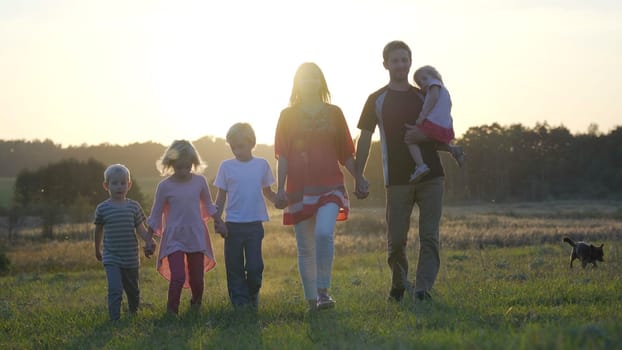 A large friendly family walks across the field at sunset with dog