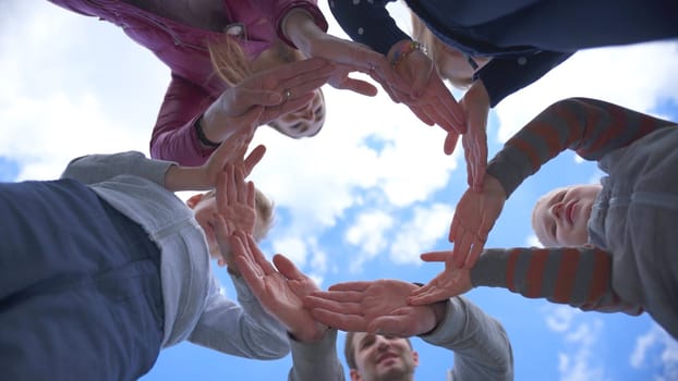 A friendly family makes a circle out of their hands against the blue sky.