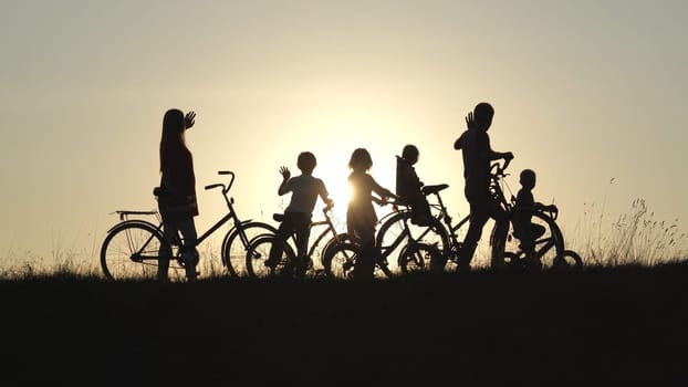 Silhouettes of a large large family waving their hands to the sun with bicycles and dogs at sunset