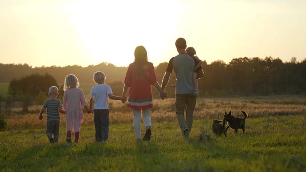 A large friendly family walks across the field at sunset with dog