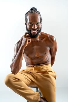 Happy african-american bearded gay man with bright makeup isolated on white background sitting chair looking at camera. Exudes sense of pride and individuality. Diversity power of personality.