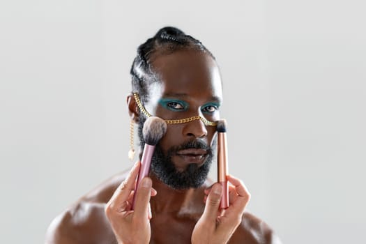 African gay applying make up holding makeup brush in hand. Close up portrait homosexual man looking at camera ready for apply visage on face. Fashion lgbt concept.