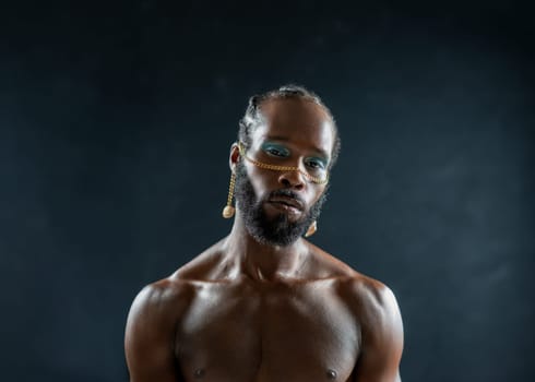 Confident african-american bearded gay man with bright makeup isolated on black, Close up portrait gay African muscular shirtless man wearing make-up looking at camera.