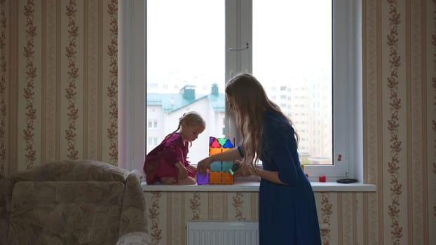 A young mother plays with her daughter in an apartment by the window