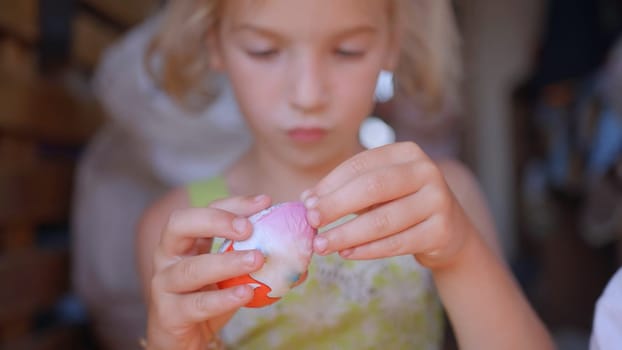 A little girl unfolds and eats a chocolate egg with toys