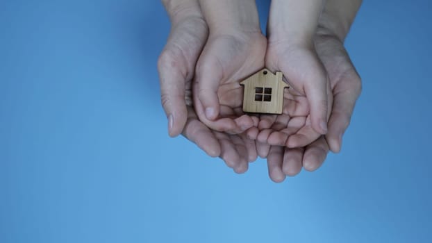 The concept of saving a friendly family. The hands of the mother and father with the child hold the figure in the form of a house