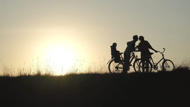 The newlyweds in love kiss with the child on the bicycles during the sunset