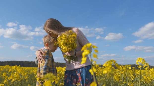 A loving son gives his mother rapeseed flowers in a rapeseed field