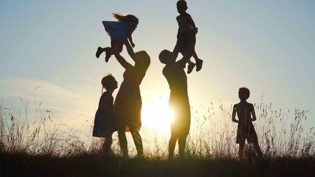 Happy parents toss their children up against the sunset