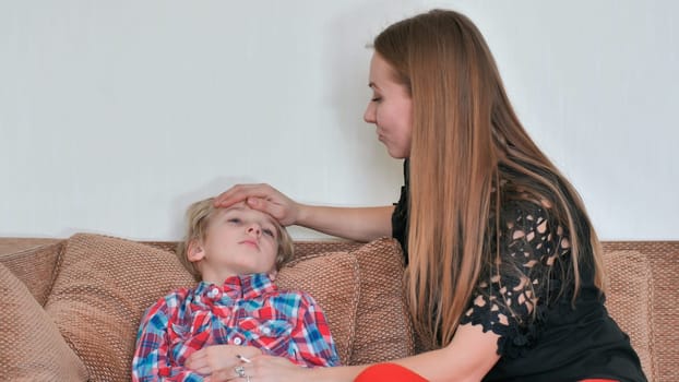 A caring mother measures the temperature of her son with a thermometer