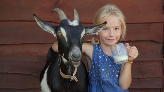 The girl drinks goat milk from a mug and hugs her beloved goat