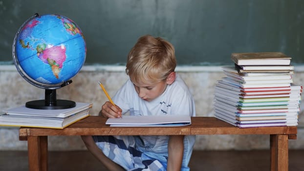 A boy of 8 years old does homework against a background of the globe. Home school concept