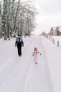 Mother and a little girl walk along a snowy road in a village at the edge of the forest. High quality photo