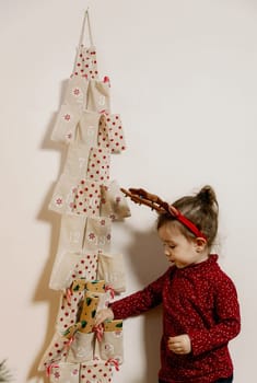 One little Caucasian girl takes out a gift from the pocket of a wall advent calendar with her hand, close-up side view.