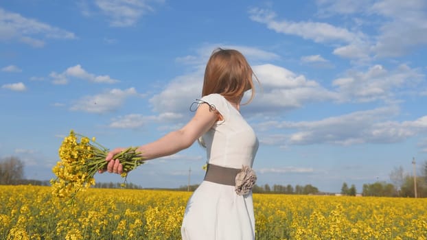 Happy girl in a white dress with a bouquet of rapeseed flowers in a yellow rapeseed field