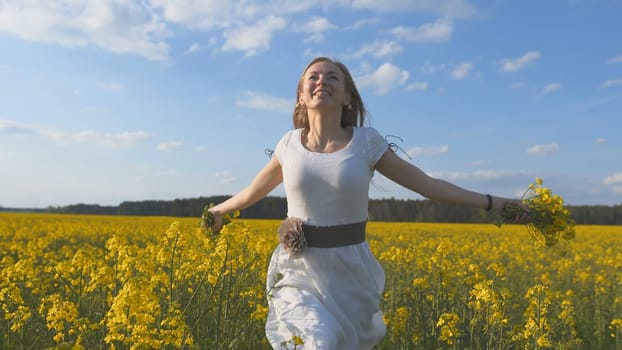 A girl in a white dress runs among a rapeseed field