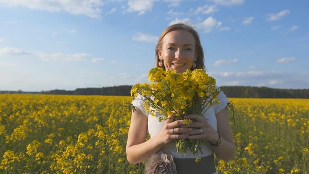 Happy girl in a white dress with a bouquet of rapeseed flowers in a yellow rapeseed field