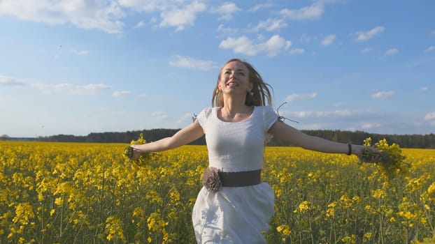 Happy girl in a white dress with a bouquet of rapeseed flowers in a yellow rapeseed field