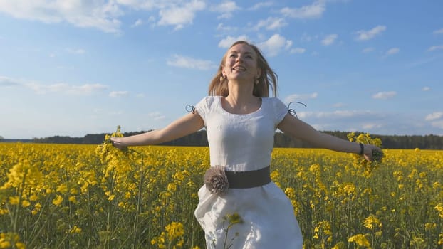 Happy girl in a white dress with a bouquet of rapeseed flowers in a yellow rapeseed field