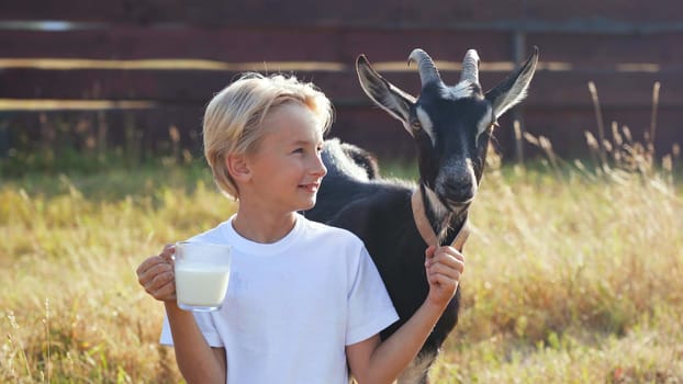 A boy drinks goat milk from a mug next to his goat