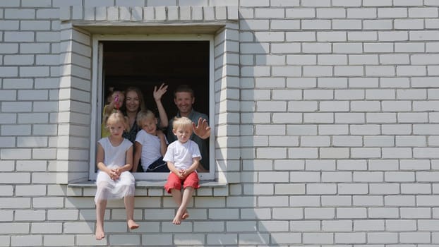 A large family waves their hands and hides from the window of their home