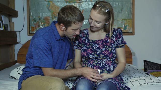 A loving husband listens to the belly of a pregnant wife with a stethoscope
