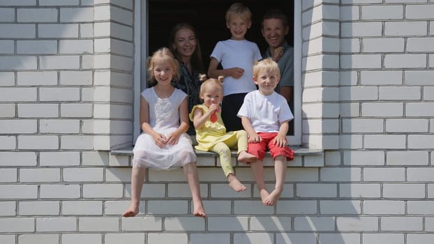 A large large family poses from the window of their home