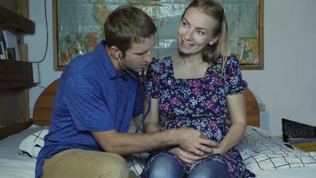 A loving husband listens to the belly of a pregnant wife with a stethoscope