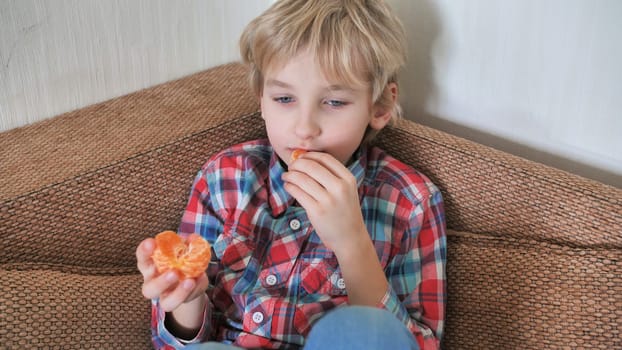 Eight year old boy eats mandarin at home.