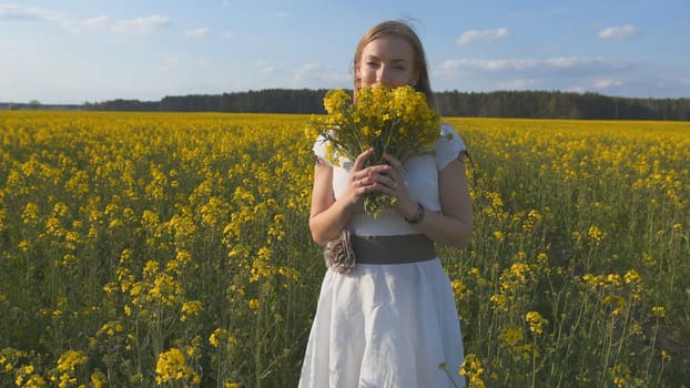 A girl in a white dress is walking among a rapeseed field