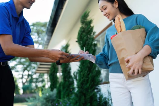 Asian woman signing the receipt on the order receipt through the online supermarket's home store.