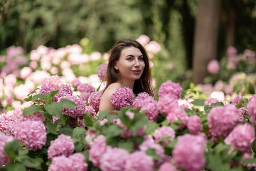 Hydrangeas Happy woman in pink dress amid hydrangeas. Large pink hydrangea caps surround woman. Sunny outdoor setting. Showcasing happy woman amid hydrangea bloom