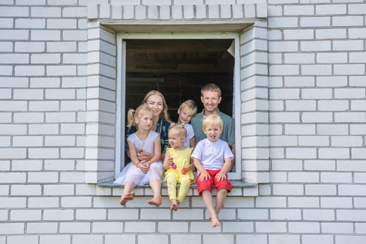A large large family poses from the window of their home