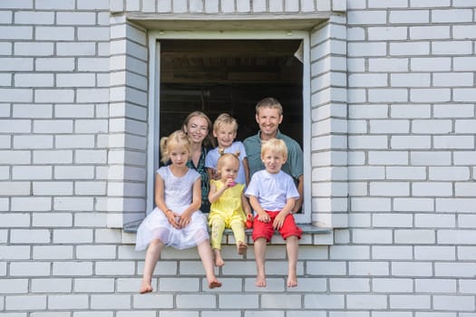 A large large family poses from the window of their home