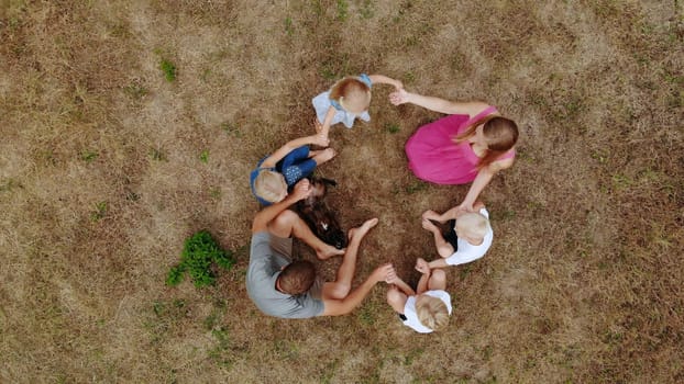 Friendly family waving hands while sitting on the grass with a dog. View from the drone