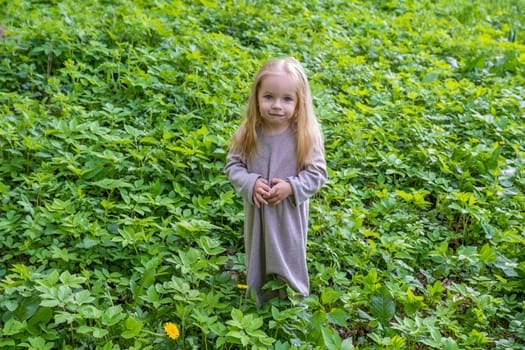 Little blonde girl in green foliage in the park