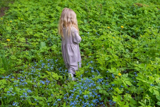 Little blonde girl in green foliage in the park