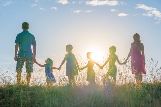 A large family is standing holding hands against the background of the sunset