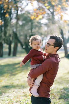 Dad is talking to a little girl in his arms in a sunny park. High quality photo