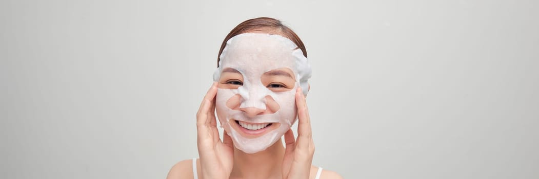 Beautiful asian woman applying paper sheet mask on her face white banner background