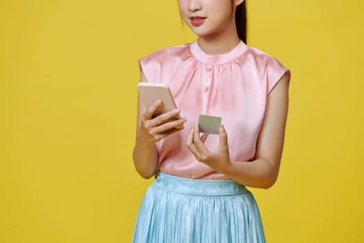 Young woman with credit card and mobile phone on color background. Online shopping