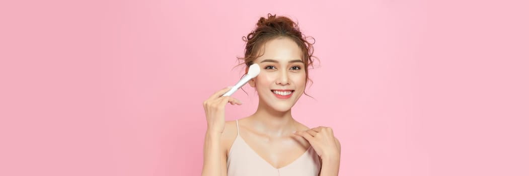 Closeup portrait of beautiful happy young girl with perfect skin is holding makeup brush in hand.