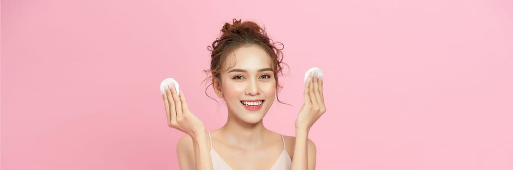 Smiling pretty young woman cleaning her face, using cotton pads and cleansing product