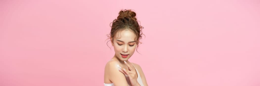Beautiful young asian woman happy applying cream or lotion with moisturizer to skin on shoulder