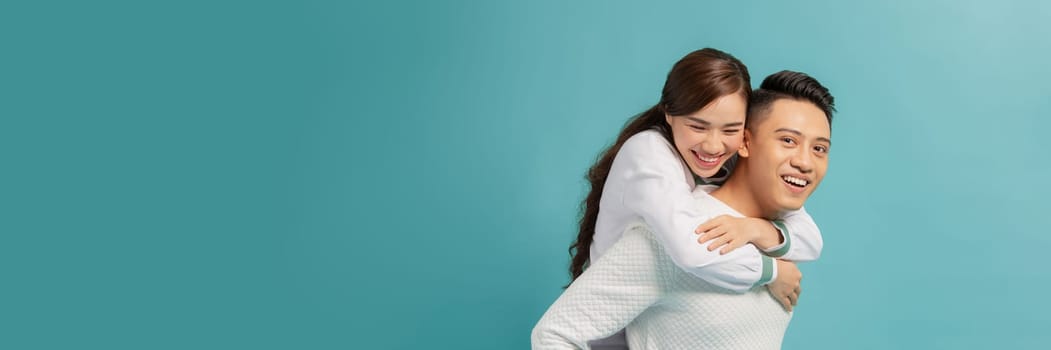 Happy smiling young asian couple piggyback isolated on light blue background