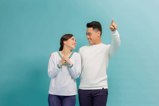 Young couple together with a big smile on face, pointing with hand finger to the side